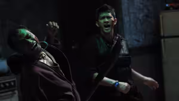 two injured men grapple in a dark room lit by green light