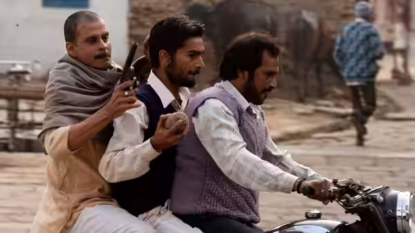 three men riding a motorcycle on a village street one holding a gun