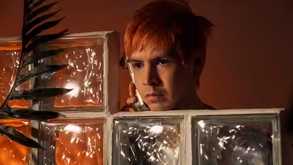 Julio Torres peering through glass blocks while holding an object