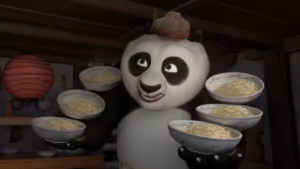 Po balances bowls of noodles in his paws inside the restaurant kitchen