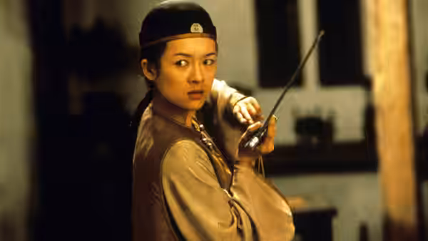 Jen (Zhang Ziyi) grips a sword while wearing a dark cap indoors