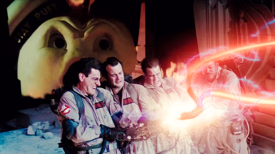 Four Ghostbusters fire proton streams before a giant Stay Puft mascot head