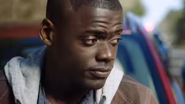 Chris (Daniel Kaluuya) looking aside with concern near a parked car