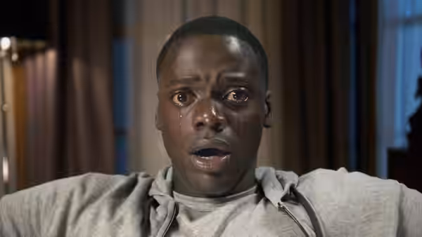 Chris (Daniel Kaluuya) with tears staring forward in a dimly lit room