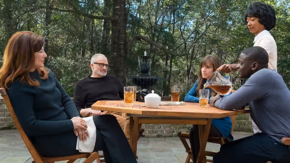 Chris (Daniel Kaluuya) pouring tea at an outdoor table with Rose and the Armitages