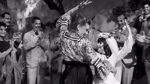 A woman in a matador costume dances with a bride as guests applaud
