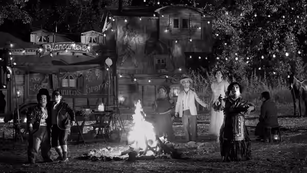 Fairground performers gather around a bonfire beneath strings of lights