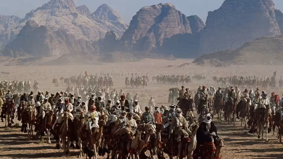 A large caravan of armed men riding camels through the desert