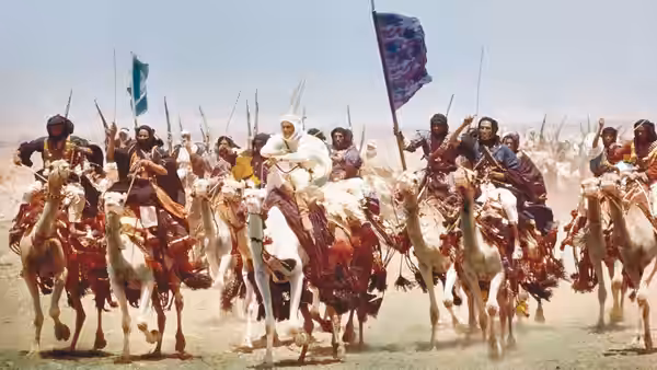 Arab fighters on camels galloping forward waving rifles and flags