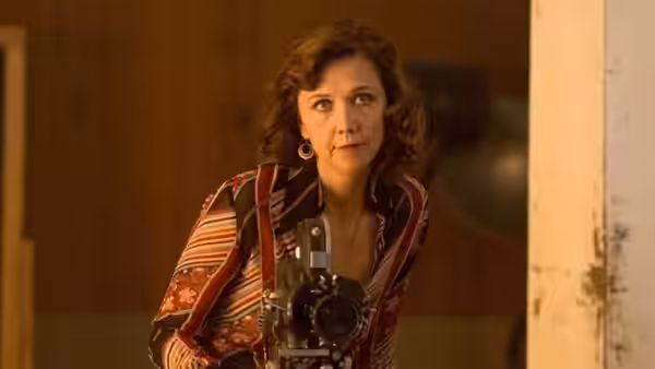 Woman holding a film camera and looking to the side inside a wooden room