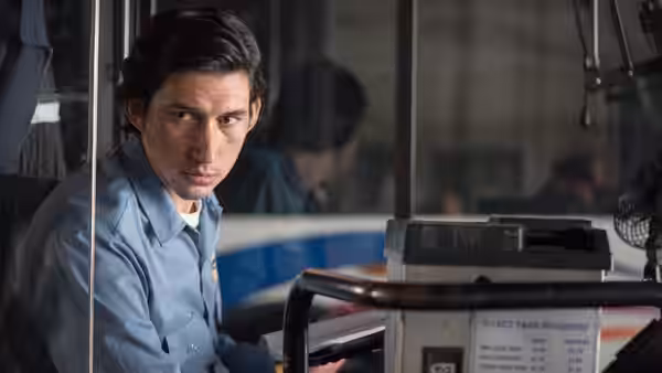 Paterson (Adam Driver) sits at the wheel of a city bus looking forward
