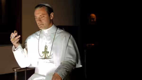 Pope Pius XIII (Jude Law) seated indoors holding a small object