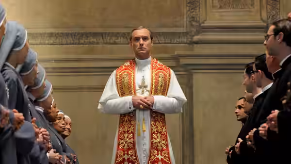 Pope Pius XIII (Jude Law) standing with hands clasped before clergy