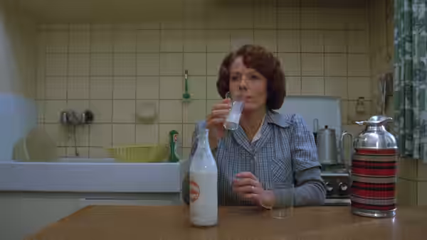 Jeanne Dielman (Delphine Seyrig) drinks from a glass in her tiled kitchen