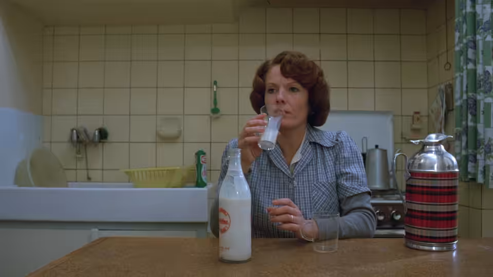 Jeanne Dielman (Delphine Seyrig) drinks from a glass in her tiled kitchen