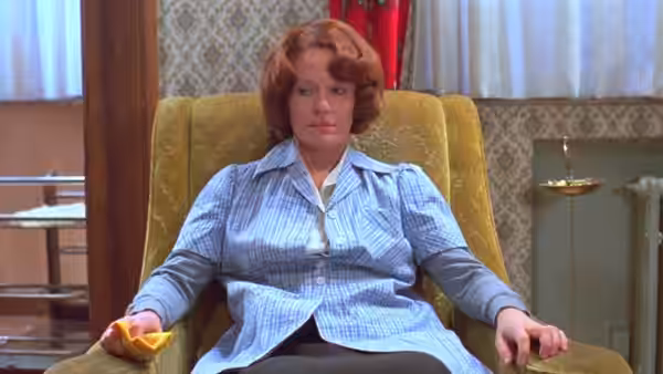 Jeanne Dielman (Delphine Seyrig) sits in an armchair holding a small yellow object