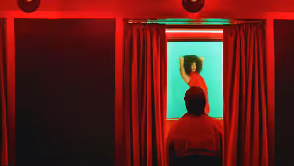person in red top seen through window as another watches from behind red curtains
