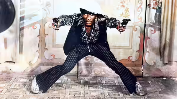 Ivan Martin (Jimmy Cliff) spreads his legs and aims a pistol inside a decorated room