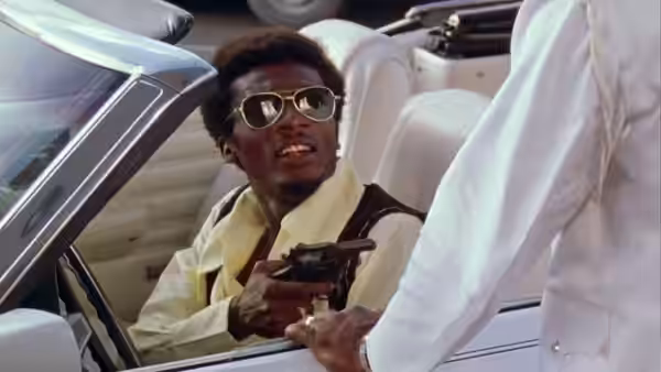 Ivan Martin (Jimmy Cliff) holds a pistol inside a car as someone reaches toward him