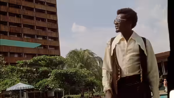 Ivan Martin (Jimmy Cliff) stands outdoors wearing sunglasses beside a tall apartment building