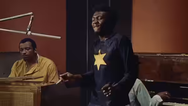 Ivan Martin (Jimmy Cliff) sings beside a seated musician in a recording studio