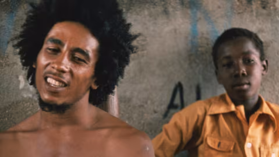 Bob Marley beside a young boy in an orange shirt against a graffiti-marked wall