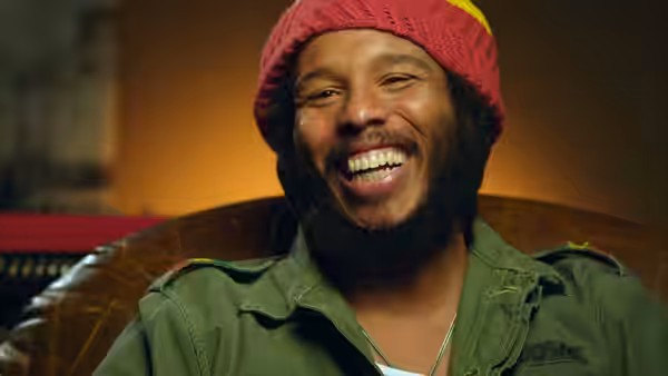 Ziggy Marley smiles in a red knit cap and green jacket