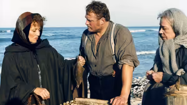 Babette (Stéphane Audran) speaks with a fisherman beside the sea as an older woman watches