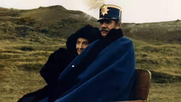 General Lorens Löwenhielm (Jarl Kulle) sits wrapped in a blanket beside a woman on open heathland