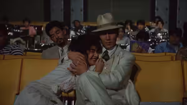 The White Suit Man (Koji Yakusho) embraces a woman in a crowded cinema