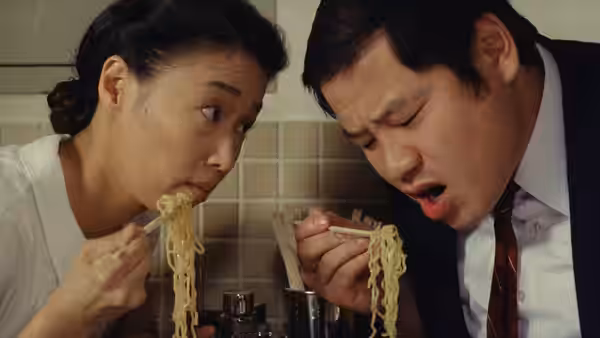 A woman and a man lean over bowls, eating noodles with chopsticks