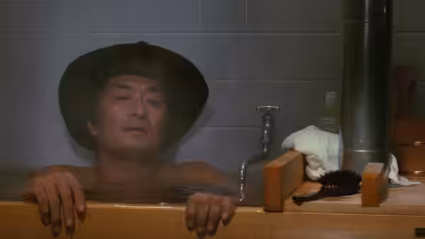 Goro (Tsutomu Yamazaki) relaxes in a wooden bath beneath a wide-brimmed hat