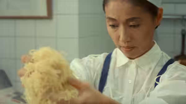 A woman in a kitchen uniform handles a tangled bundle of noodles