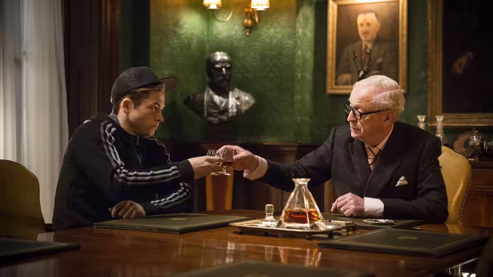 Eggsy (Taron Egerton) meets Arthur (Michael Caine) across a desk in the Kingsman office