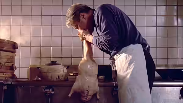 A cook leans over a duck in a tiled kitchen