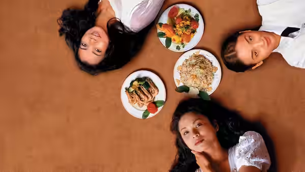 Three women lie around plates of food arranged on the floor
