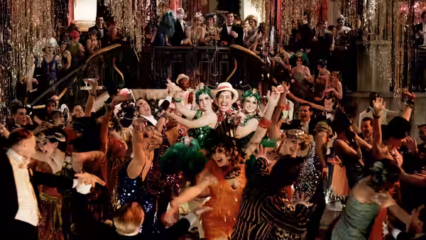 Partygoers dance and cheer beneath glittering decorations at Gatsby’s crowded mansion