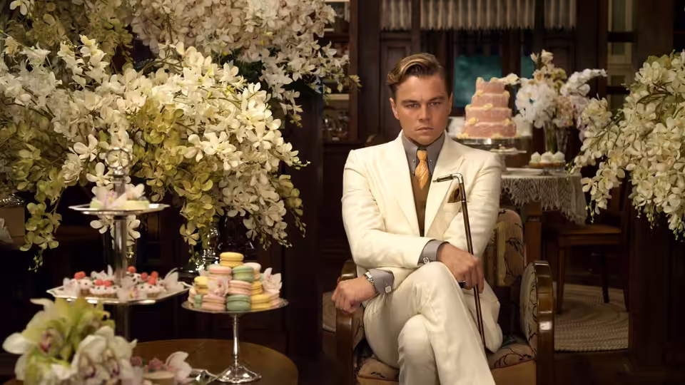 Jay Gatsby (Leonardo DiCaprio) sits among flowers and tiered trays of tea-party sweets