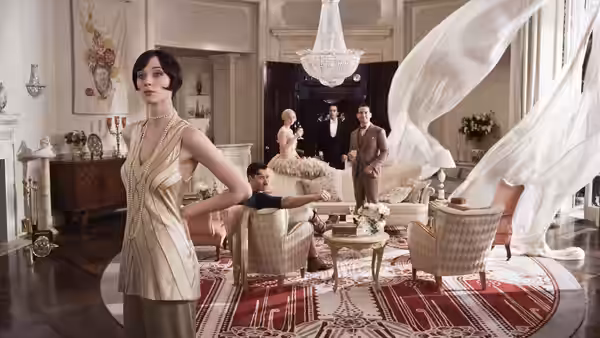 Jordan Baker stands in the foreground as guests gather in a bright, flower-filled living room
