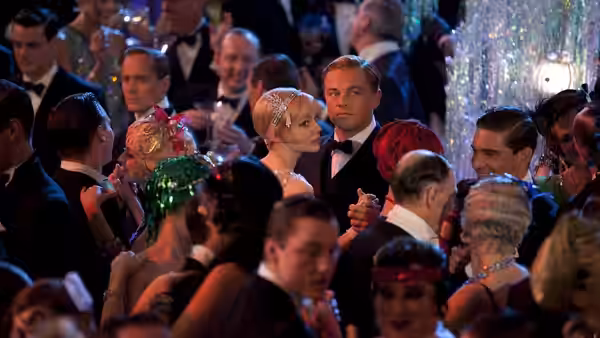 Jay Gatsby and Daisy Buchanan dance together amid guests at a crowded party