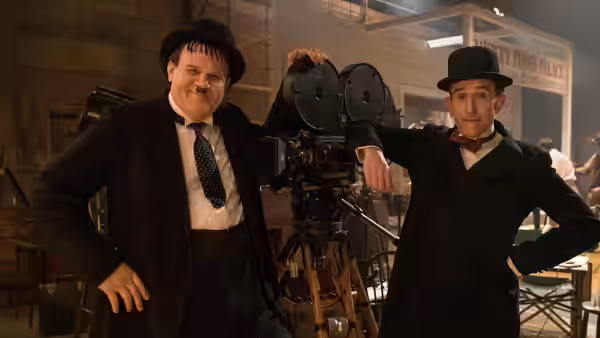 Stan Laurel (Steve Coogan) and Oliver Hardy (John C. Reilly) pose beside a vintage film camera