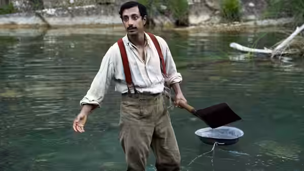 Hermann Kermit Warm (Riz Ahmed) stands in a river holding a pan