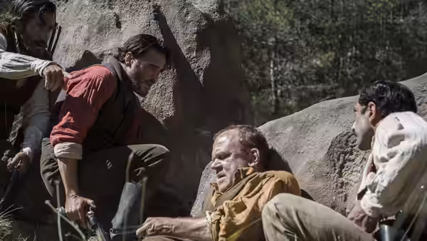 Eli Sisters sits against a boulder as two men gather beside him
