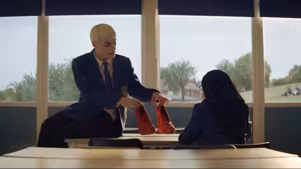 Jamie New (Max Harwood) shows red high heels to Pritti Pasha in a classroom