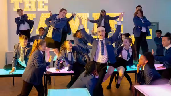 Jamie New (Max Harwood) dances with classmates in a brightly lit school hall