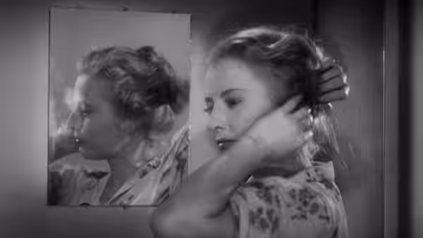 Stella Dallas (Barbara Stanwyck) fixes her hair while looking in a mirror