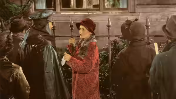 A woman in a red coat holds a hat among customers and hat stands