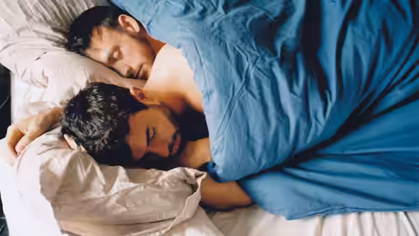 Two men sleeping together in bed under blue covers
