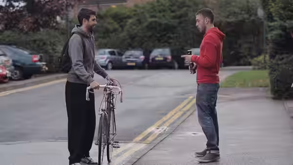 Two men standing on a street one holding a bicycle