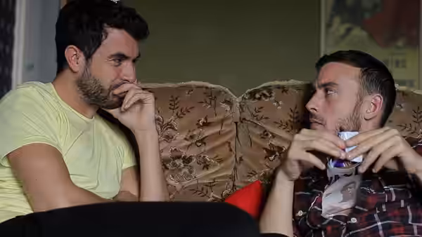 Two men sitting on a couch talking one holding a mug
